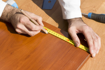 Stolarz odmierza odległość za pomocą miary i zaznacza za pomocą ołówka stolarskiego. - obrazy, fototapety, plakaty