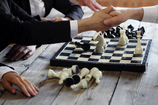 People shaking hands over chessboard