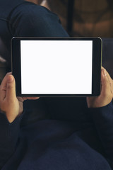 Mockup image of woman's hand holding black tablet pc with blank white screen on thigh with floor background in modern cafe