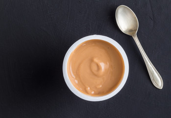 Yogurt background top view shot of caramel flavoured yoghurt in plastic cup with small silver spoon...
