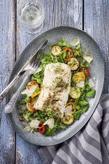 Fried cod fish fillet with lettuce and vegetable with white wine as top view on a plate