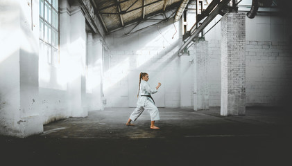 Caucasian female in Kimono practicing karate, Japanese martial arts. Old warehouse indoor shot © supamotion