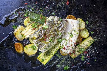 Fried cod fish fillet with vegetable and potatoes as top-view on old metal sheet