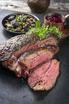 Barbecue haunch of venison with mushrooms and cranberry sauce as close-up on a slate slab