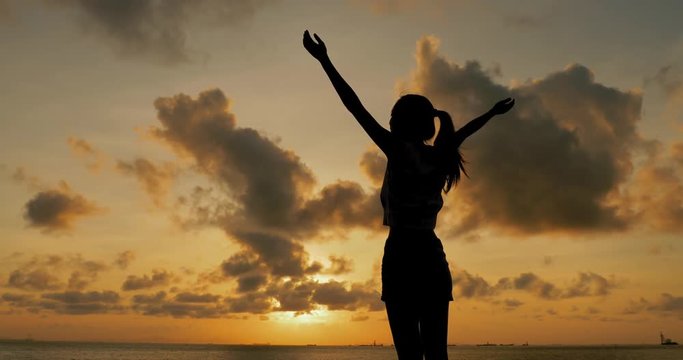 Silhouette of woman raise hand up under sunset