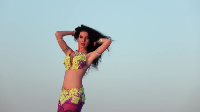 Professional dancer in a shiny suit makes sexual movements against the blue sky