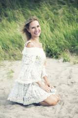 Fototapeta na wymiar blond woman in white dress sitting on the beach