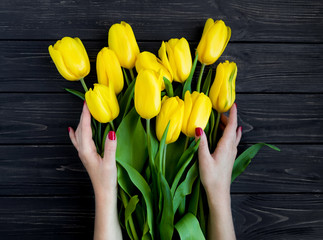 Female hands holding yellow tulips on black vintage wooden table. Flat lay, top view