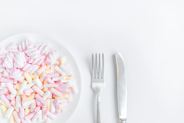 Colorful light marshmallows on a plate on white background. Top view, flat lay