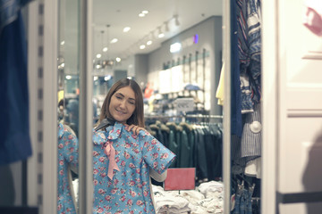 happy asian woman choosing clothes and looking to mirror in mall or clothing store