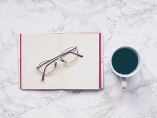 Black coffee and open notebook or journal with glasses on marble background. Flat lay. Top view. Copy space