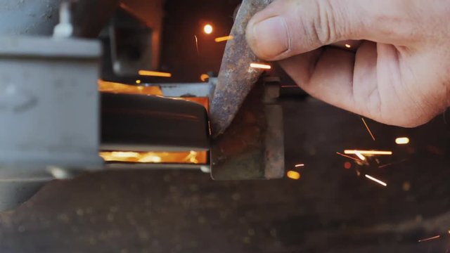 Worker sharpening tools by grinding wheel. Extreme close up. Slow motion