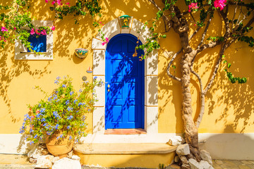 Blue door of a yellow Greek house decorated with flowers, Assos town, Kefalonia island, Greece
