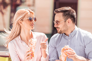 Couple enjoying lunch sitting at bench in city.
