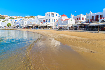 Fototapeta na wymiar MYKONOS PORT, GREECE - MAY 16, 2016: View of beautiful beach and restaurants on shore in Mykonos town, Mykonos island, Greece.