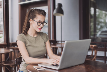 Business wooman using laptop at cafe. Young beautiful girl sitting in a coffee shop and working on...