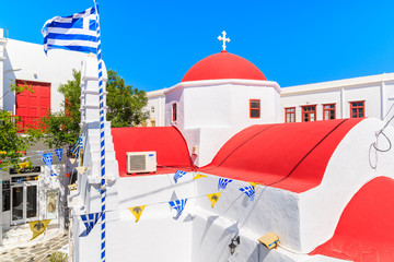 MYKONOS ISLAND, GREECE - MAY 17, 2016: Church building with red roof and Greek flag on whitewashed street in beautiful Mykonos town, Cyclades islands, Greece. © pkazmierczak