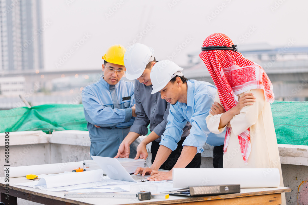 Wall mural Arabian businessman and Engineer and Laborer working and discussion with laptop  on construction plans front of building in his work site. Teamwork concept - Wall murals