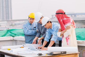 Arabian businessman and Engineer and Laborer working and discussion with laptop  on construction plans front of building in his work site. Teamwork concept