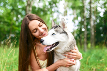 Happy young woman sitting with her dog siberian husky  on grass in park