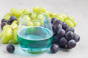 Trendy blue moscato wine in a glass, green and red grape on background, horizontal