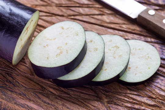 Eggplant and eggplant slices on wooden cutting board, horizontal