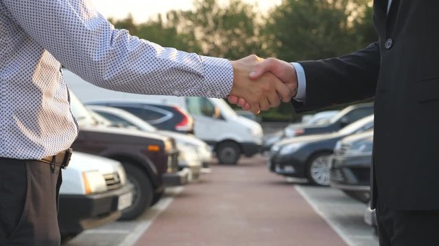 Male hands in suit giving keys of car to his friend. Arm of businessman passes car key. Handshake between two business men outdoor. Close up Slow motion