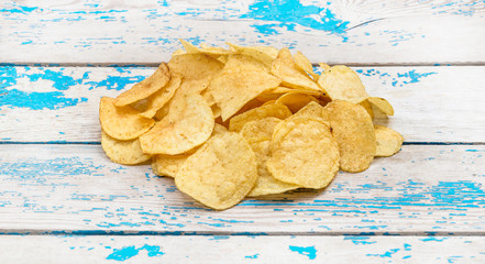 Heap of potato chips on the wooden background.