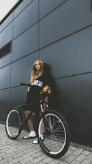 Outdoor lifestyle portrait of pretty sexy lookin young girl in hockey jersey style dress posing on gray wall background with street bicycle