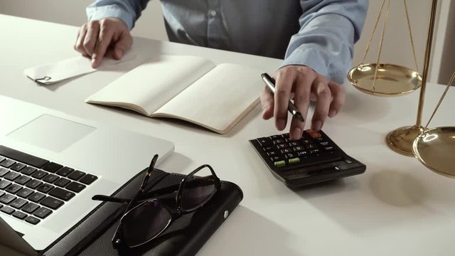 justice and law concept.businessman or lawyer or accountant working on accounts using a calculator and laptop computer and documents in 4k (UHD)