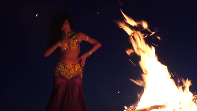 Late night a girl in the sand dancing belly dancing near a bright campfire