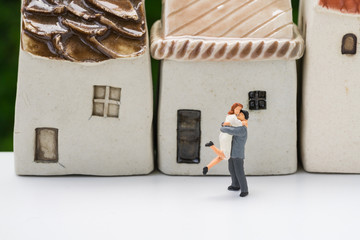 Miniature happy couple family standing with ceramic house as property or financial mortgage plan concept