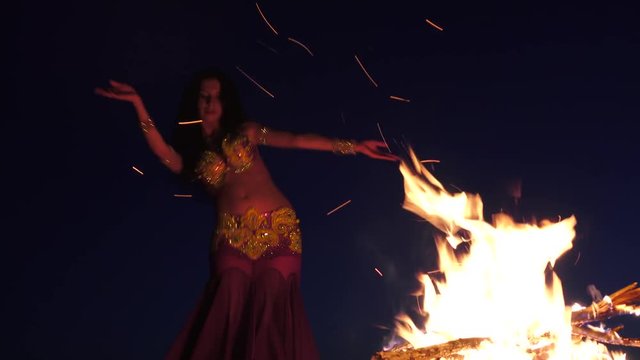 Girl in the sand dancing belly dancing near a bright campfire