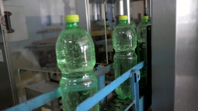 Automatic conveyor line for bottling mineral water in the green plastic bottle. Line for PET bottle water. Water factory-bottling pure spring water into bottles. Selective focus.