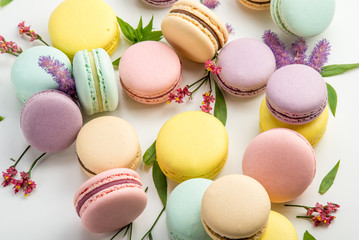 Colorful macarons with leaves and red flowers on a white background. French delicate dessert