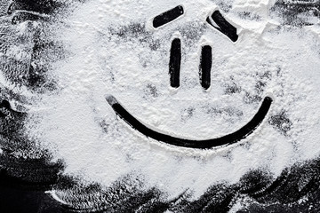 Smiley on white wheat flour at abstract black background