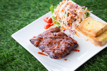 Close up view of pork barbecue ribs with barbecue sauce that served with garlic bread and vegetable salad.