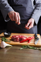 Chef seasoning rib eye steak on wooden board at restaurant kitchen