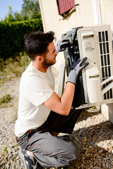 young man electrician installer working on outdoor compressor unit air conditioner at a client's...