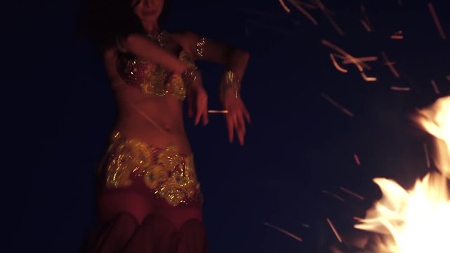 Night the girl dances belly dancing on the sand, she has a bright outfit