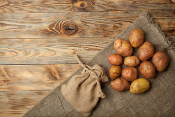 Raw potato food . Fresh potatoes in an old sack on wooden background. Free place for text. Top view