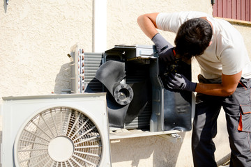 young man electrician installer working on outdoor compressor unit air conditioner at a client's...