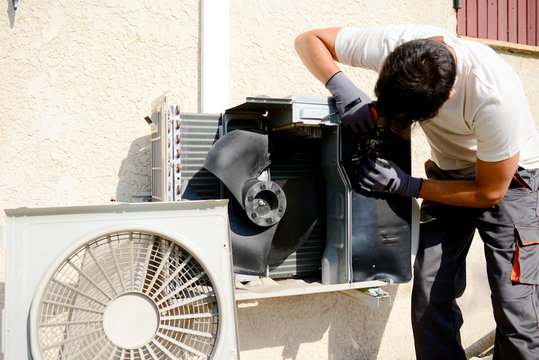 Young Man Electrician Installer Working On Outdoor Compressor Unit Air Conditioner At A Client's Home