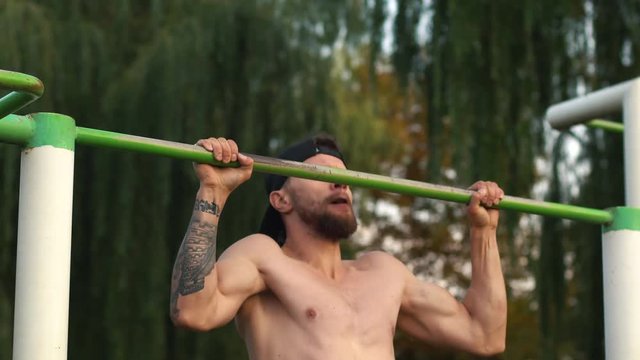 young bearded man pulls himself up on a bar in the park