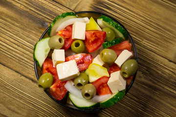 Greek salad in glass bowl on wooden table