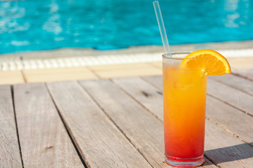 Glasses with colored cocktails on the side of a swimming pool with blue water in the background