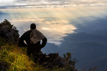 A traveler on top of mountain, he sitting on the rock watching a nice sunrise