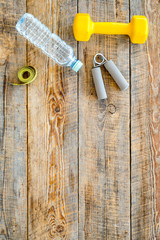 Fitness for losing weight. Dumbbells, expander, measure tape and water on wooden background top view copyspace