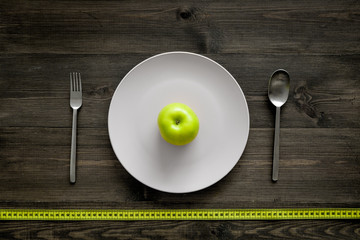 Slimming diet. Apple at plate and measuring tape on wooden background top view