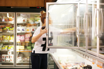  Woman choosing frozen food from a supermarket freezer